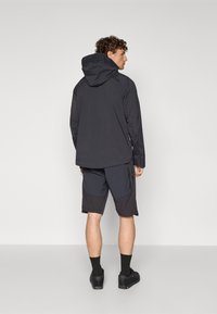 Chaqueta ligera negra con capucha, combinada con pantalones cortos oscuros con un patrón texturizado. Calzado casual completa el look.