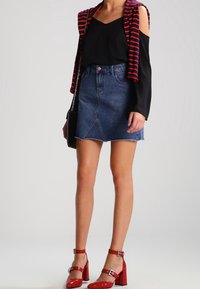 Denim mini sukně s překříženým designem, černý top s odhalenými rameny a červené šněrovací boty na blokovém podpatku. Vzorovaný červený a černý cardigan.