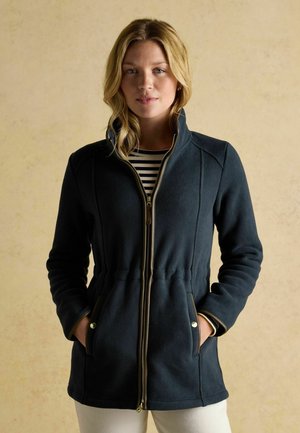 Dark navy fleece jacket with a high collar, gold zipper, and tapered silhouette. Features side pockets and contrast stitching.