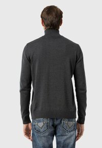 Grauer, langärmeliger Pullover mit hohem Kragen und gerippten Bündchen; getragen über blauen Jeans mit detaillierter Steppung an den Gesäßtaschen.