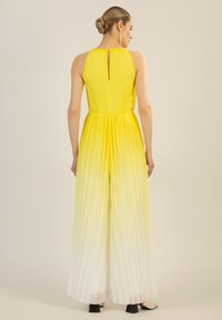 Mono amarillo con pliegues, de cuello alto, cintura ceñida y degradado que se desvanece a blanco en la parte inferior. Presenta un detalle en forma de ojal en la parte posterior.