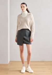 Beige, fluffy genser, grå omslagsskjørt og hvite joggesko. Strukturert strikk, V-hals design og synlige detaljer. Enkelt, moderne silhuett.