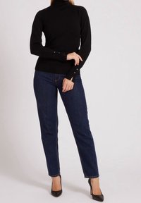 Pull à col roulé noir avec des manches longues et des accents de boutons, associé à un jean droit bleu foncé et des escarpins noirs.