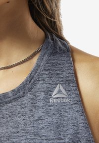 Šedý sportovní tílko s texturovaným vzorem, na hrudi se stříbrným logem Reebok a s designem na zádech ve stylu racerback.