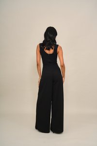 Must kombinesoon laia säärega, keha järgiva ülaosaga ja kaardus seljaga. Sile kangas ja peened õmblusdetailid, mis loovad vooluva silueti.