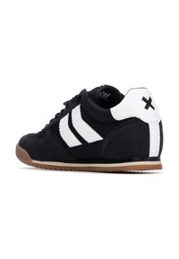 Zapatilla deportiva negra con rayas blancas, parte superior de ante y textil, suela de goma y un talón blanco en contraste con un acento negro.