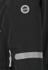 Giacca nera con un patch del logo argento, dettagli riflettenti e una tasca con zip sul lato per funzionalità e visibilità.