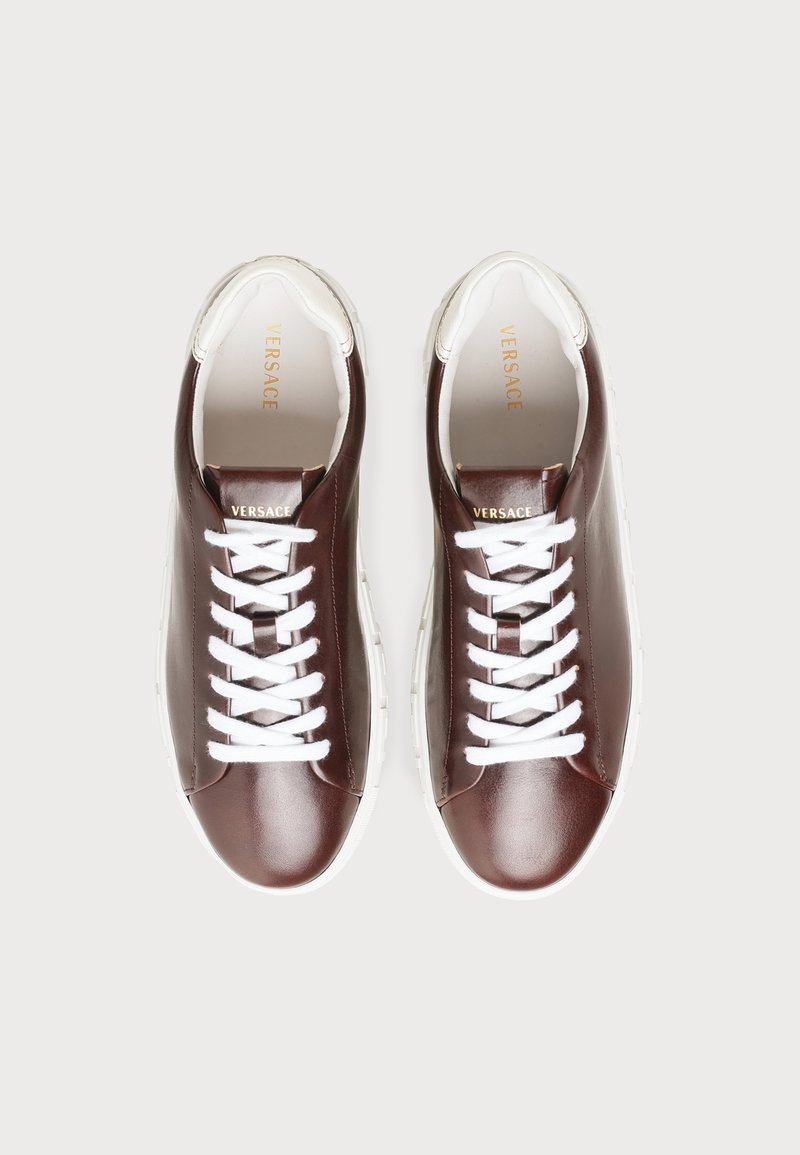 Pair of brown leather sneakers with white laces and soles, Versace branding on tongue and inner sole, viewed from above on a gray background.