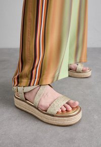 Gold glitter platform sandals with two wide straps. The sole is natural woven jute with a shiny golden footbed, highlighting the foot.