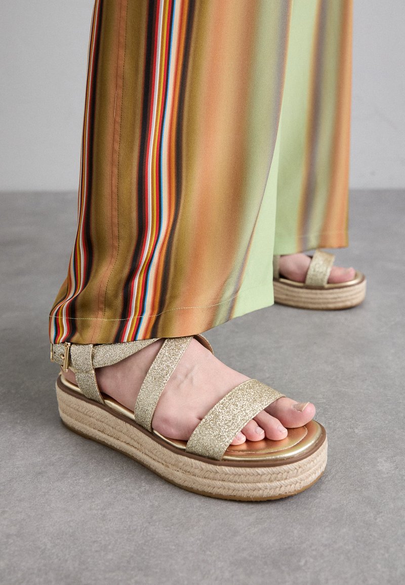 Gold glitter platform sandals with two wide straps. The sole is natural woven jute with a shiny golden footbed, highlighting the foot.