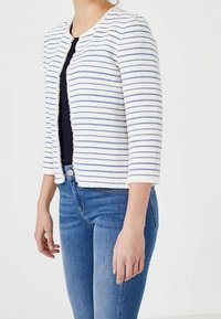 Valkoinen ja siniraitainen neuletakki, jossa on kolme neljäsosan mittaiset hihat, pyöreä pääntie ja teksturoitu kangas. Edessä avoin malli, jossa on käänteettömät reunat.