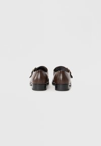 Zapatos de cuero marrón con textura de cocodrilo, de forma redondeada y con un tacón pequeño. Presentan una correa decorativa con una hebilla de metal.