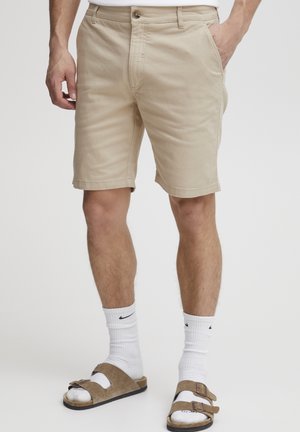 Beige katoenen shorts met een flat front, riemlussen en een ritssluiting. Draag ze met witte crew sokken en bruine sandalen met dubbele gespen.