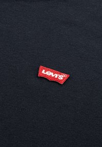 Svart bomull t-skjorte med en rød brodert Levi's-logoet på halsen, liggende på en jevn, flat stoffoverflate.