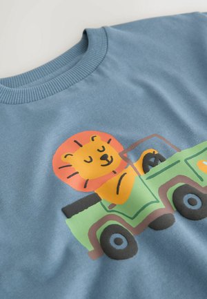 Blaues Sweatshirt mit einem bunten Motiv eines Löwen, der einen grünen Lastwagen fährt, mit einem gerippten Halsausschnitt und glatter Stoffstruktur.