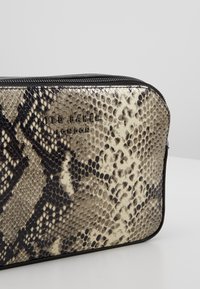 Obdélníková zipová taštička s černým a béžovým hadím vzorem, sytě vystouplé logo "Ted Baker London" na přední straně.