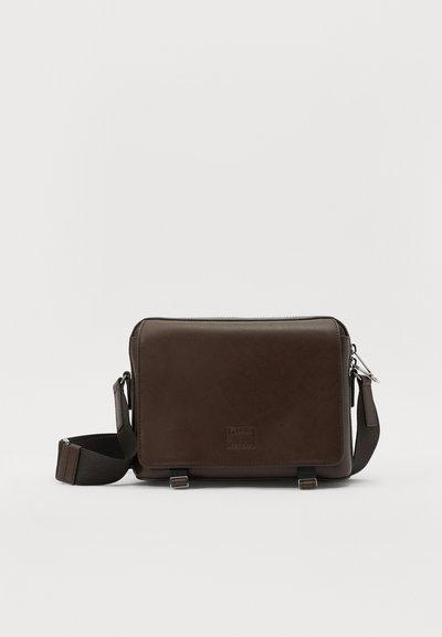 Brown leather messenger bag with a smooth texture, rectangular shape, adjustable strap, silver hardware, and front logo detail.