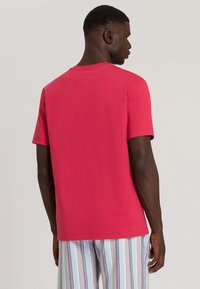 T-shirt rosso a maniche corte in cotone morbido, con collo rotondo e design semplice. Cuciture visibili sulle maniche e sull'orlo.