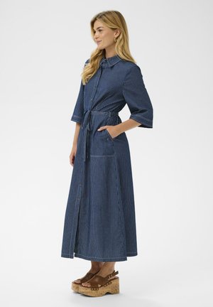 Farmeringruha függőleges fehér csíkokkal, galléros nyakkivágással, háromnegyedes ujjakkal, deréknál megkötős, oldalzsebekkel. Fa platform szandál.