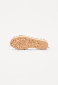 Kengän pohja, jossa on vaalean beige väri, teksturoitu kuvio ja kukkakoristeita. Muotoilu sisältää kudotun yläosan.
