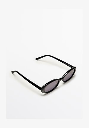 Schwarze ovale Sonnenbrille mit schlanken Bügeln und dunkel getönten Gläsern, präsentiert auf weißem Hintergrund.