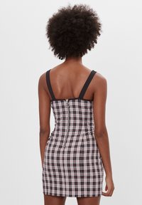 Rutig mini-klänning med en figursydd design. Har ett svart och vitt rutmönster, justerbara axelband och en dragkedja bak i mitten.