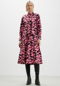 Abito a fiori in rosa e nero, con collo alto, maniche lunghe, corpetto aderente e gonna a strati. Abbinato a stivali neri sopra il ginocchio.