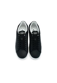 Black sneaker with a smooth synthetic finish, featuring flat black laces, a white sole, and a logo on the tongue and side.