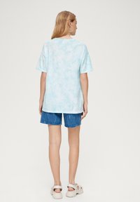 Lichtblauwe tie-dye T-shirt van zachte stof, met korte mouwen en een losse pasvorm, gecombineerd met denim shorts en sandalen.