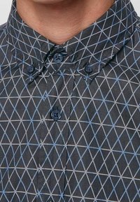 Overhemd met knoopsluiting in donkere stof met een geometrisch patroon van blauwe en grijze driehoeken. Bevat een kraag en knoopaccenten.