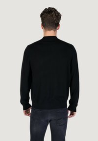Maglione nero a maglia con collo rotondo, maniche lunghe e orlo aderente. Il tessuto appare morbido e liscio con un design semplice e classico.