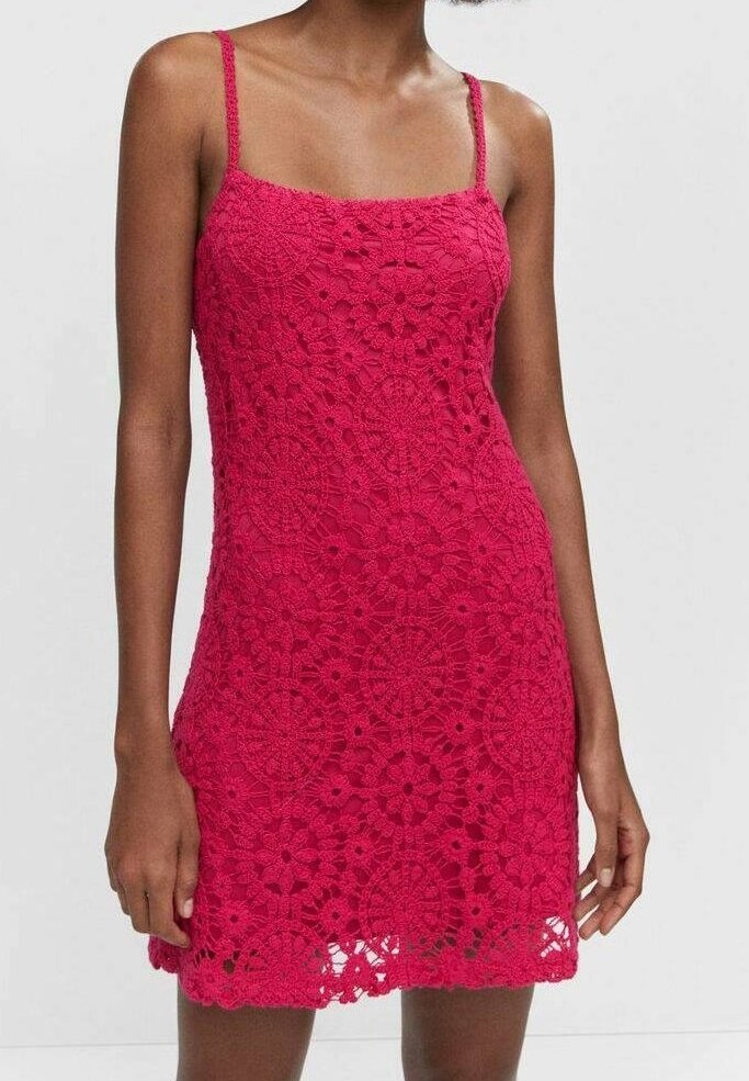 Femme portant une mini robe en crochet rose vif sans manches avec des motifs floraux et de fines bretelles.