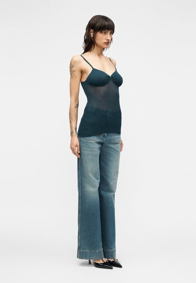 Στενή μπλούζα σε βαθύ τιρκουάζ με λ επτές τιράντες, σε συνδυασμό με ανοιχτό μπλε τζιν παντελόνι φαρδιάς γραμμής, με ευθεία κοπή και διακριτικό ξεθώριασμα.