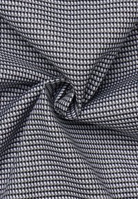 Tessuto intrecciato in bianco e nero con un motivo geometrico. La texture è liscia con una leggera lucentezza e forme quadrate distinte in tutto il tessuto.