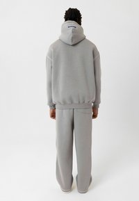 Grijze hoodie en bijpassende trainingsbroek van zachte stof, met een trekkoord in de capuchon en een achterzak op de broek.