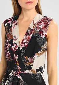 Blommig klänning med svart och beige design. Har en djup V-ringning, ärmlös skärning och bälte som accentuerar midjan. Strukturerad tyg.