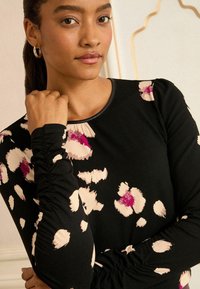 Fekete, hosszú ujjú topp rózsaszín és krémszínű absztrakt pöttyökkel, fodros ujjú kialakítással és kerek nyakkivágással.