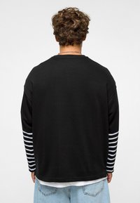 Zwarte langemouwshirt met gestreepte manchetten, ronde hals en een relaxed fit; de stof lijkt zacht met een gladde textuur en minimale details.