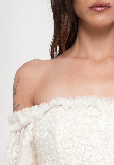 Vestido off-the-shoulder en blanco con bordado floral texturizado y detalle de volantes en el escote. Tejido ligero y transparente con un suave drapeado.