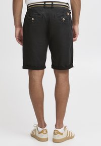 Pantaloni shorts neri con risvolti, dotati di tasche posteriori con chiusura a bottone. Un cinturino a righe multiple aggiunge un dettaglio di contrasto.