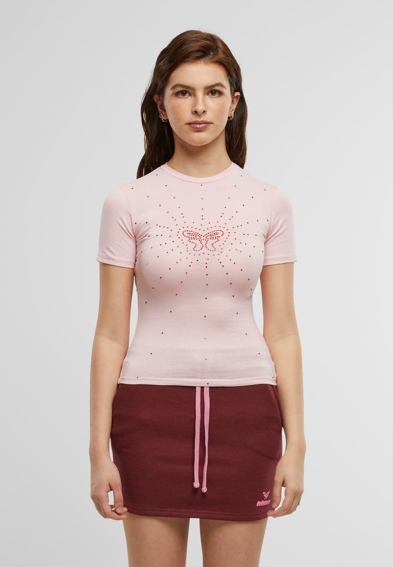 Rosa tettskjorte med korte ermer som har et sommerfugldesign og rhinestones. Brukt sammen med et burgunder skjørt og kontrasterende snor.