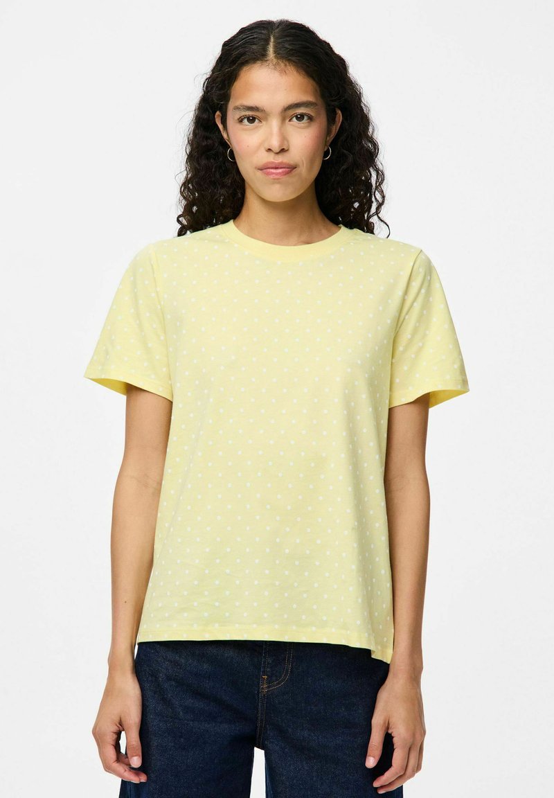 Gul bomullströja med korta ärmar, prydd med vita prickar. Rund halsringning och avslappnad passform. Kombinerad med mörkblå jeans.