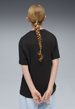 Schwarzes Baumwoll-T-Shirt mit entspannter Passform, kurzen Ärmeln und langen, blonden Haaren, die zu einem Zopf geflochten sind. Der Hintergrund ist ein grauer Farbverlauf.