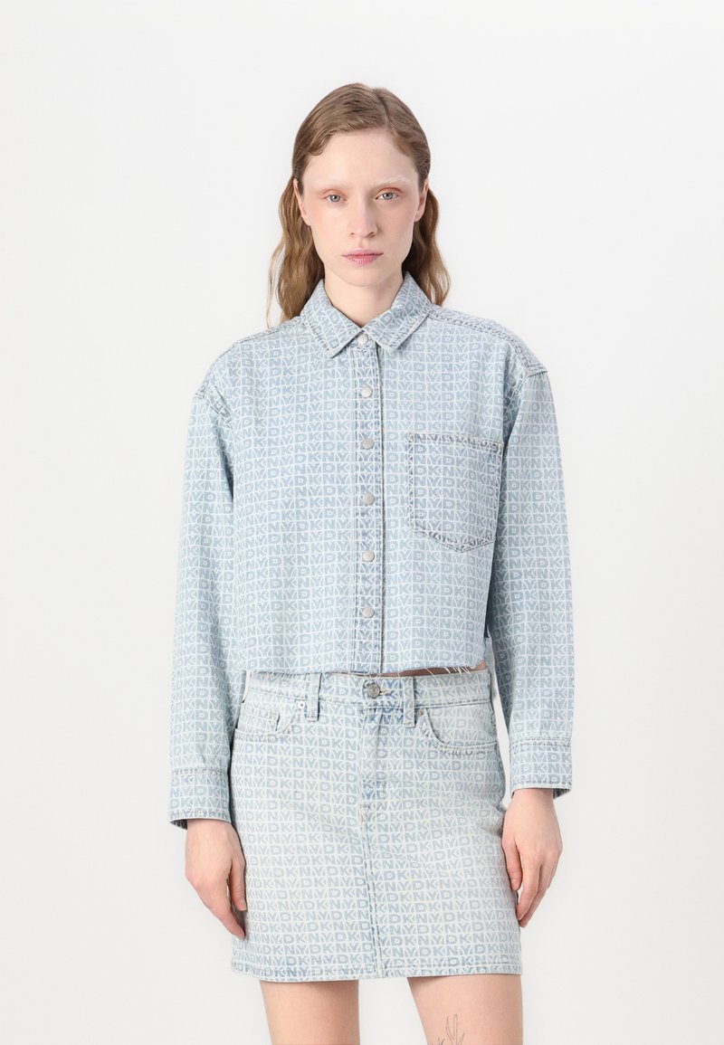 Cropped denim jacket and skirt set in light blue with a repeating pattern, featuring a button closure, collar, and front pocket detail.