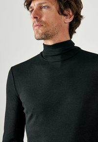 Zwarte coltrui van ribbelstof, met lange mouwen en een aansluitende pasvorm. Gladde textuur met een hoge hals.