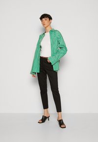 Zeleno-bíle pruhovaná oversized košile, bílé přiléhavé tričko, černé úzké kalhoty a černé muly na podpatku. Jednoduchý, čistý design.