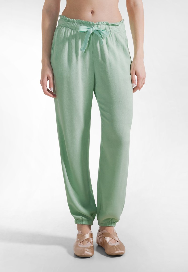 Pantalones de tela suave de color verde claro con cintura fruncida y lazo ajustable. Los puños son elásticos. Combinados con bailarinas beige.