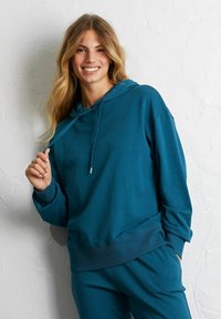 Felpa con cappuccio in teal realizzata in tessuto morbido, con orli a coste, coulisse regolabile e vestibilità comoda e rilassata.