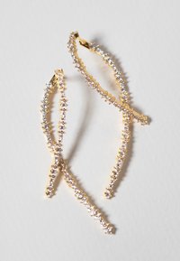 Orecchini d'oro con design ondulato allungato, adornati con piccoli cristalli trasparenti lungo i bordi, creando un effetto scintillante.