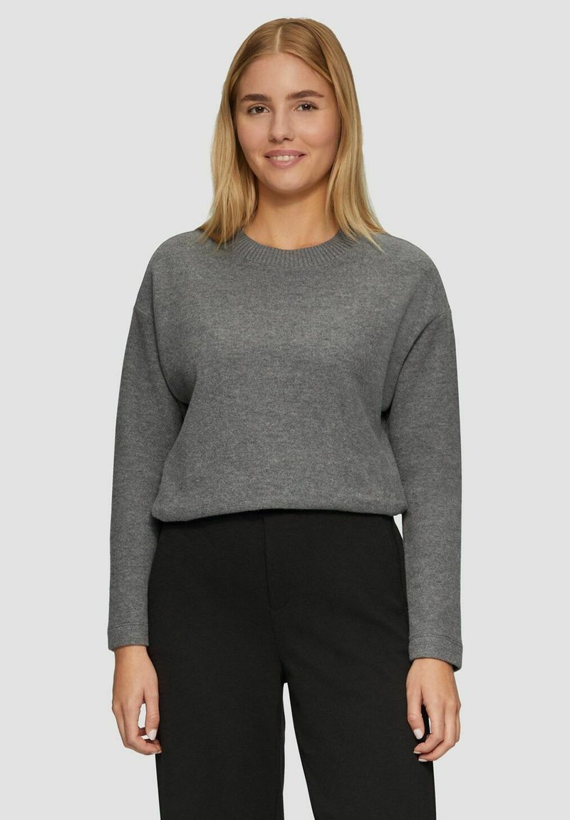 Grauer, übergroßer Pullover mit Rundhalsausschnitt und langen Ärmeln, aus weichem Stoff, kombiniert mit schwarzen Hosen.